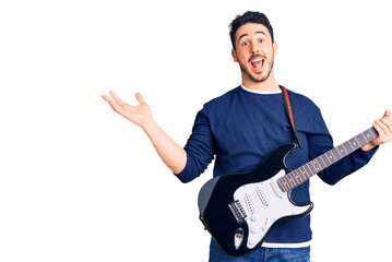 Young hispanic man playing electric guitar celebrating victory with happy smile and winner expression with raised hands
