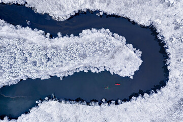 Kayaking on river between snowy forest. Extreme Sport in winter.