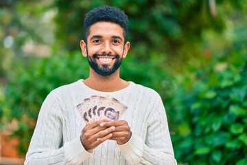 Young african american man smiling happy holding mexican 500 pesos banknotes at the park.