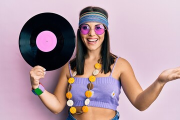 Young brunette woman wearing hippie style holding vinyl disc celebrating achievement with happy...