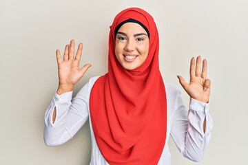 Young beautiful hispanic girl wearing traditional islamic hijab scarf showing and pointing up with...