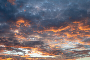 Orange and black  cotton-textured clouds spread across a blue sky to the horizon
