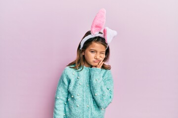 Little beautiful girl wearing cute easter bunny ears touching mouth with hand with painful...