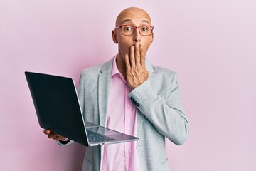 Bald man with beard holding laptop covering mouth with hand, shocked and afraid for mistake....