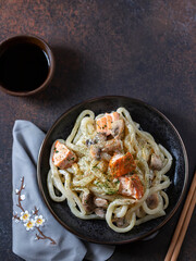 Udon, wheat noodles, with Skewered Salmon and mushrooms on a dark background.