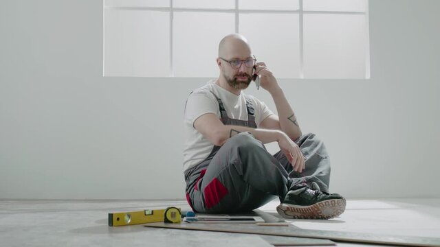 Builder with glasses calls on mobile phone sitting on floor