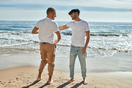 Young gay couple smiling happy dancing at the beach.