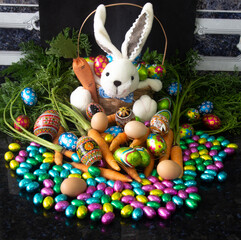 Easter rabbit amidst many chocolate eggs and carrots