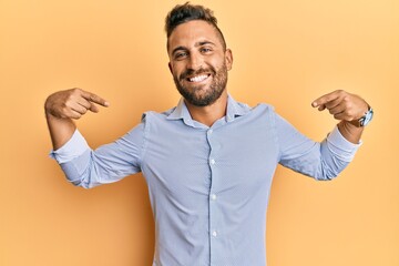 Handsome man with beard wearing casual clothes looking confident with smile on face, pointing...
