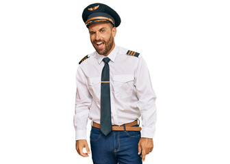 Handsome man with beard wearing airplane pilot uniform winking looking at the camera with sexy expression, cheerful and happy face.