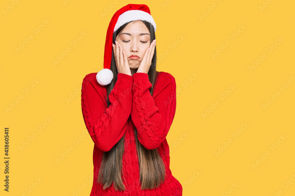 Sticker young chinese woman wearing christmas hat tired hands covering face, depression and sadness, upset a