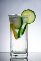 London dry gin and schweppes indian tonic in highball glass filled with glass with few slices of fresh cutted cucumber and lemon. Vegetable on the side. Reflected surface and gradient background.