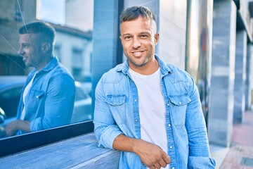 Young caucasian man smiling happy leaning on the wall at the city.