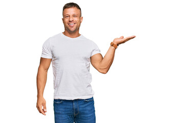 Handsome muscle man wearing casual white tshirt smiling cheerful presenting and pointing with palm of hand looking at the camera.
