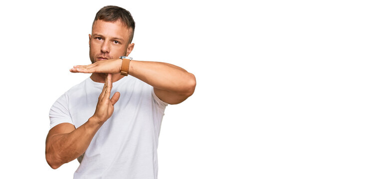 Handsome muscle man wearing casual white tshirt doing time out gesture with hands, frustrated and serious face