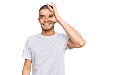 Hispanic young man wearing casual white t shirt doing ok gesture with hand smiling, eye looking through fingers with happy face.