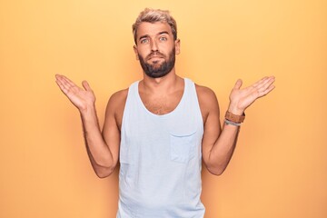 Young handsome blond man wearing casual sleeveless t-shirt over isolated yellow background clueless and confused with open arms, no idea and doubtful face.