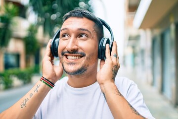 Young hispanic man smiling happy listening to music using headphones at street of city.