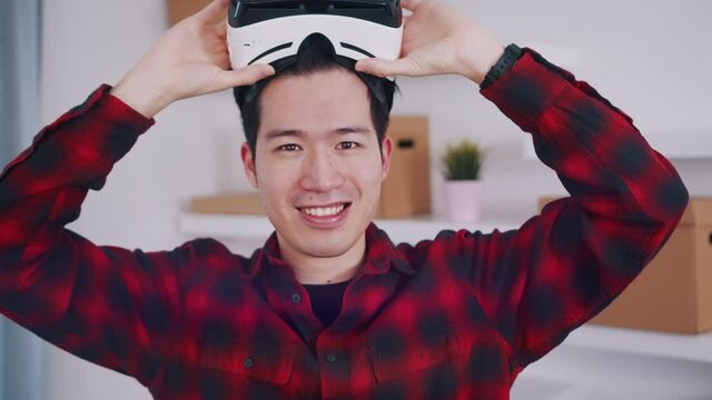 Asian young man removing VR headset from hs eyes and smiling. High quality 4k footage