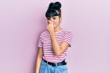 Young hispanic girl wearing casual clothes smelling something stinky and disgusting, intolerable...