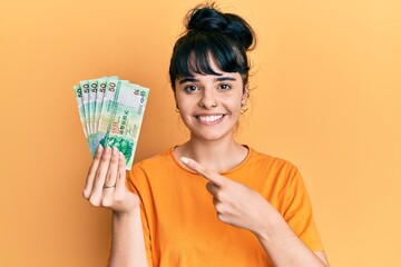 Young hispanic girl holding 50 hong kong dollars banknotes smiling happy pointing with hand and finger