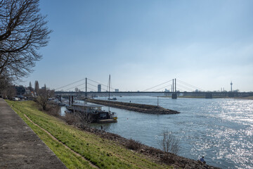 Outdoor sunny view along promenade riverside, pier and harbour on Rhine River and background cityscape, suspension bridge and Rhine tower in Düsseldorf, Germany.