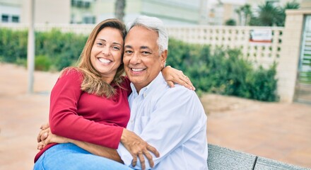Naklejka premium Middle age hispanic couple smiling happy and hugging sitting on the bench.