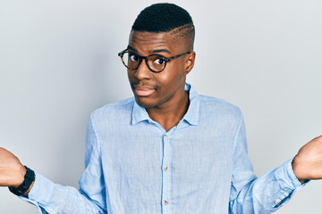 Young african american man wearing casual clothes and glasses clueless and confused with open arms, no idea and doubtful face.