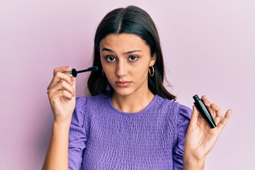 Young hispanic woman holding eyelashes curler skeptic and nervous, frowning upset because of...