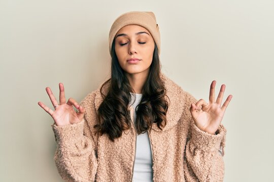 Young hispanic woman wearing wool sweater and winter hat relax and smiling with eyes closed doing meditation gesture with fingers. yoga concept.