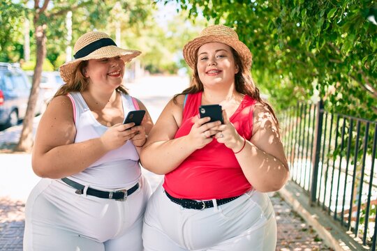 Two plus size overweight sisters twins women with smartphone outdoors on a sunny day