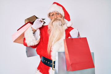 Old senior man with grey hair and long beard wearing santa claus costume holding shopping bags depressed and worry for distress, crying angry and afraid. sad expression.
