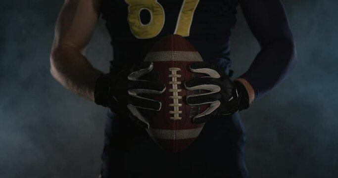 American football sportsman player holding a ball on black background close up