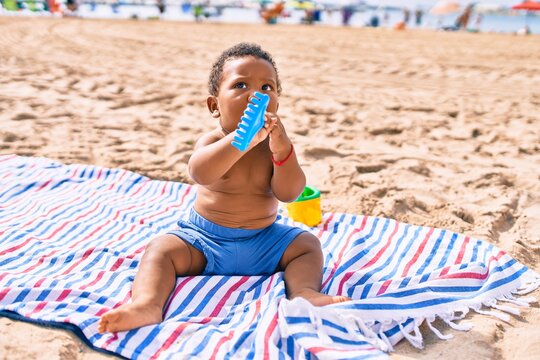 Adorable african american toddler playing with toys sitting on the sand at the beach.