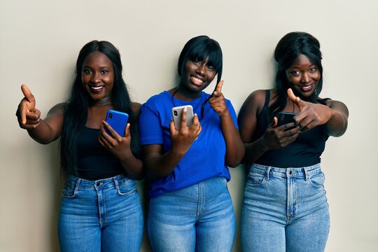 Three young african american friends using smartphone pointing fingers to camera with happy and funny face. good energy and vibes.