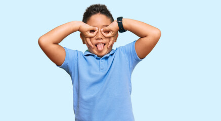 Little boy hispanic kid wearing casual clothes doing ok gesture like binoculars sticking tongue out, eyes looking through fingers. crazy expression. © Krakenimages.com