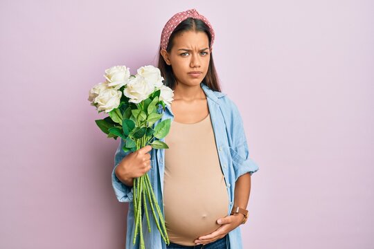 Beautiful hispanic woman expecting a baby holding flowers skeptic and nervous, frowning upset because of problem. negative person.