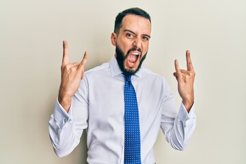 Young man with beard wearing business tie shouting with crazy expression doing rock symbol with hands up. music star. heavy concept.