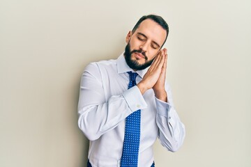 Young man with beard wearing business tie sleeping tired dreaming and posing with hands together while smiling with closed eyes.