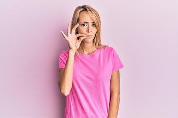 Beautiful blonde woman wearing casual pink tshirt mouth and lips shut as zip with fingers. secret...