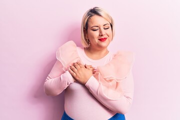 Young beautiful blonde plus size woman wearing casual sweater over isolated pink background smiling with hands on chest, eyes closed with grateful gesture on face. Health concept.