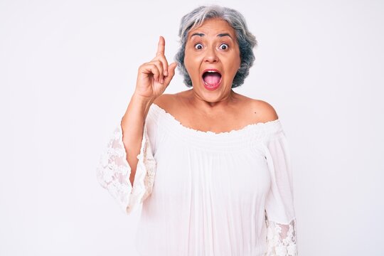 Senior hispanic grey- haired woman wearing casual clothes pointing finger up with successful idea. exited and happy. number one.