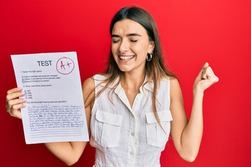 Young hispanic woman showing a passed exam holding trophy screaming proud, celebrating victory and success very excited with raised arm