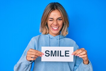 Beautiful caucasian woman holding smile text winking looking at the camera with sexy expression, cheerful and happy face.
