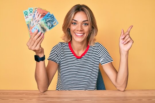 Beautiful caucasian woman holding australian dollars smiling happy pointing with hand and finger to the side