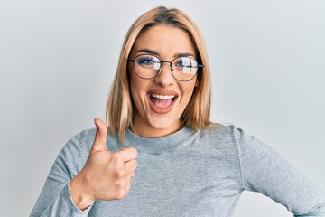 Young caucasian woman wearing casual clothes and glasses smiling happy and positive, thumb up doing excellent and approval sign