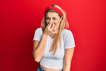 Young caucasian woman wearing casual white t shirt smelling something stinky and disgusting,...