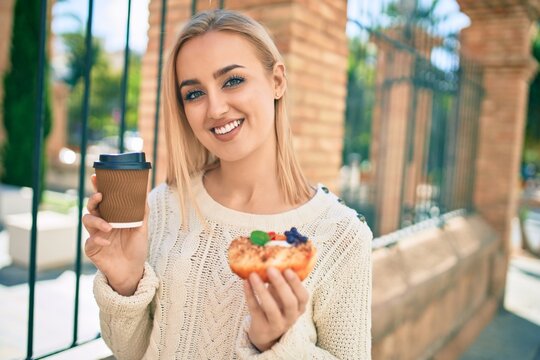Young blonde girl smiling happy having breakfast standing at the city.