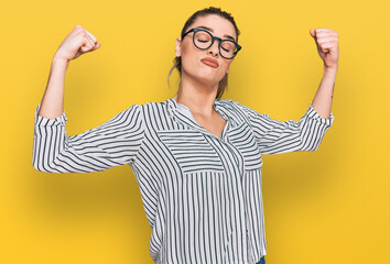 Young caucasian woman wearing business shirt and glasses showing arms muscles smiling proud. fitness concept.