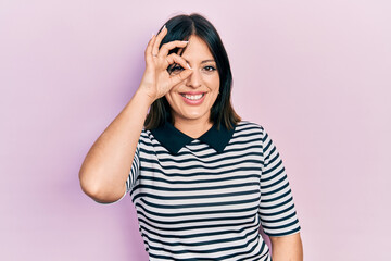 Young hispanic woman wearing casual clothes doing ok gesture with hand smiling, eye looking through fingers with happy face.